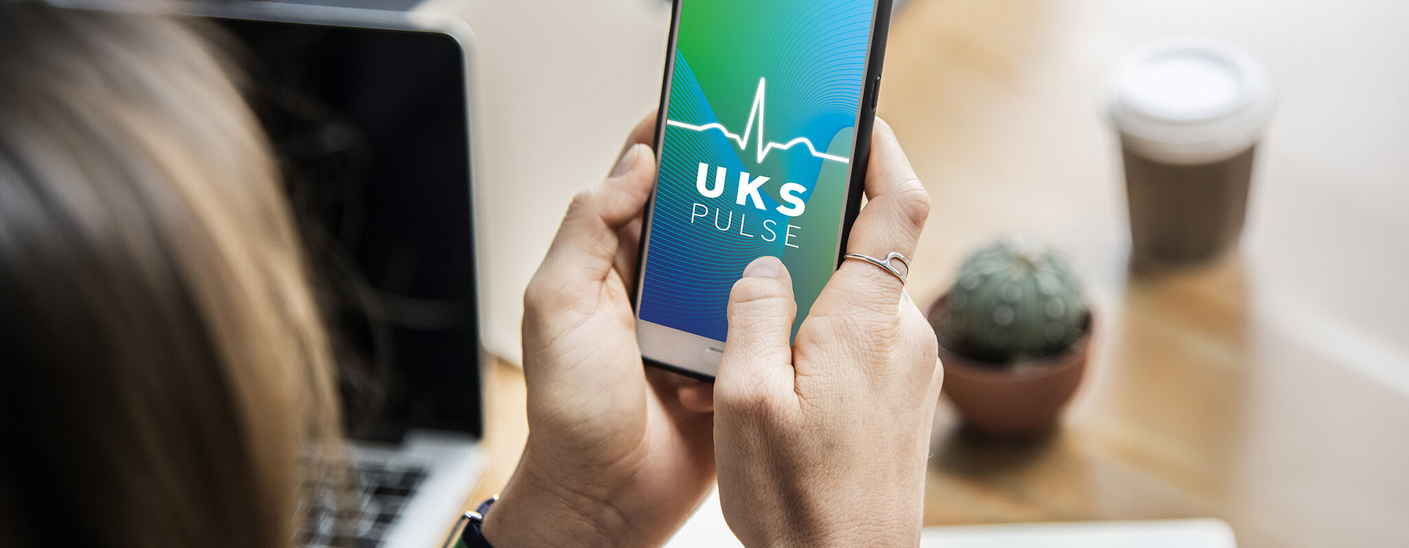 Webbanner zum Launch der UKS-App, Block über die Schulter, eine Frau hält Ihr Smartphone in der rechten Hand und ruft die UKS-App auf
